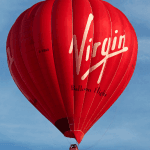 A Virgin red hot air balloon in a bright blue sky.