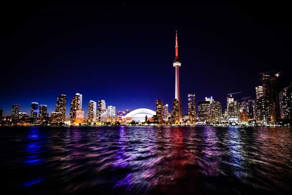 The iconic skyline of downtown Toronto, Ontario as seen from the waters of Lake Ontario at night, with the world-renowned CN Tower towering above skyscrapers and tall buildings.