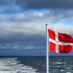 A flag on a pole near the sea under a cloudy sky.