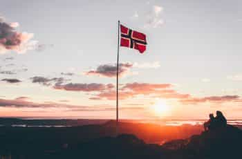 A flag hoisted on a rocky terrain against a sunset.