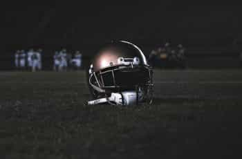 The helmet of an American football player sitting on the field with two teams seen off in the background.