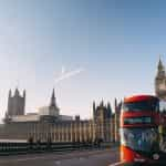 A red bus passing across the bridge in front of Westminster in London, UK.